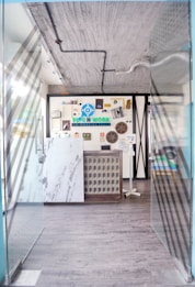 A modern entrance to a co-working space featuring glass doors with diagonal patterns, leading into a room with a decorative wall. The wall includes various objects and an eye-catching logo for the space. The floors are wooden and there are visible industrial-style ceiling fixtures.