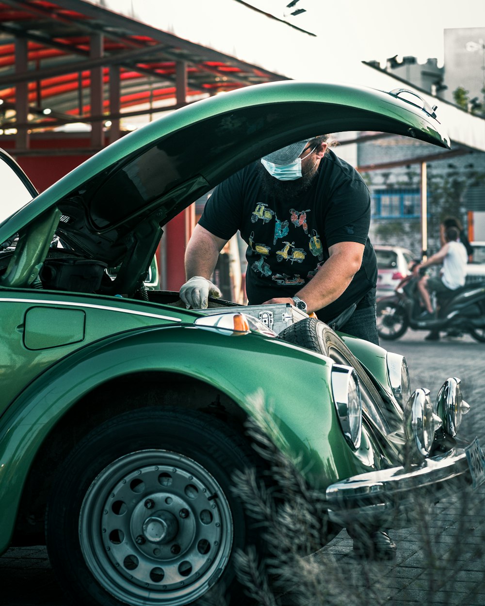 man in black t-shirt and white pants standing beside green car