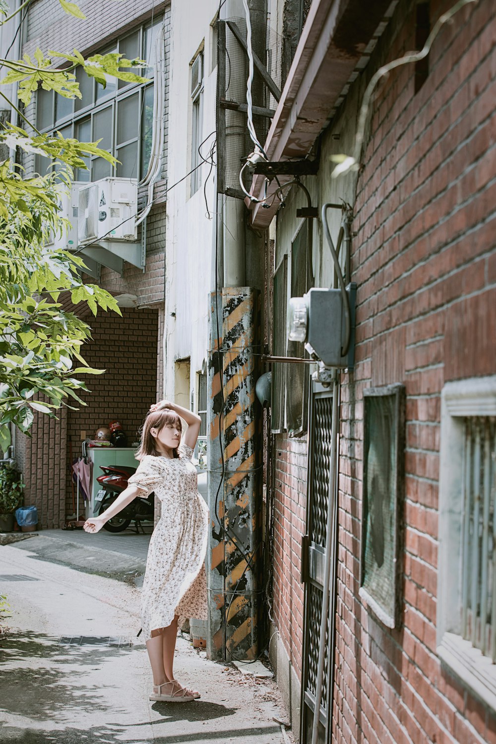 woman in brown and white floral dress standing beside brown brick building during daytime