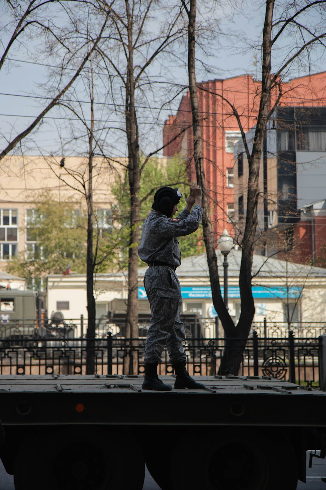 man in black jacket and pants standing on black metal fence near bare trees during daytime