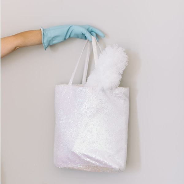 Woman in blue rubber cleaning glove holds up white sequin bag with a lambswool duster.by Katie Pearse