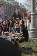 An energetic drummer surrounded by a crowd of smiling listeners on a busy sidewalk.