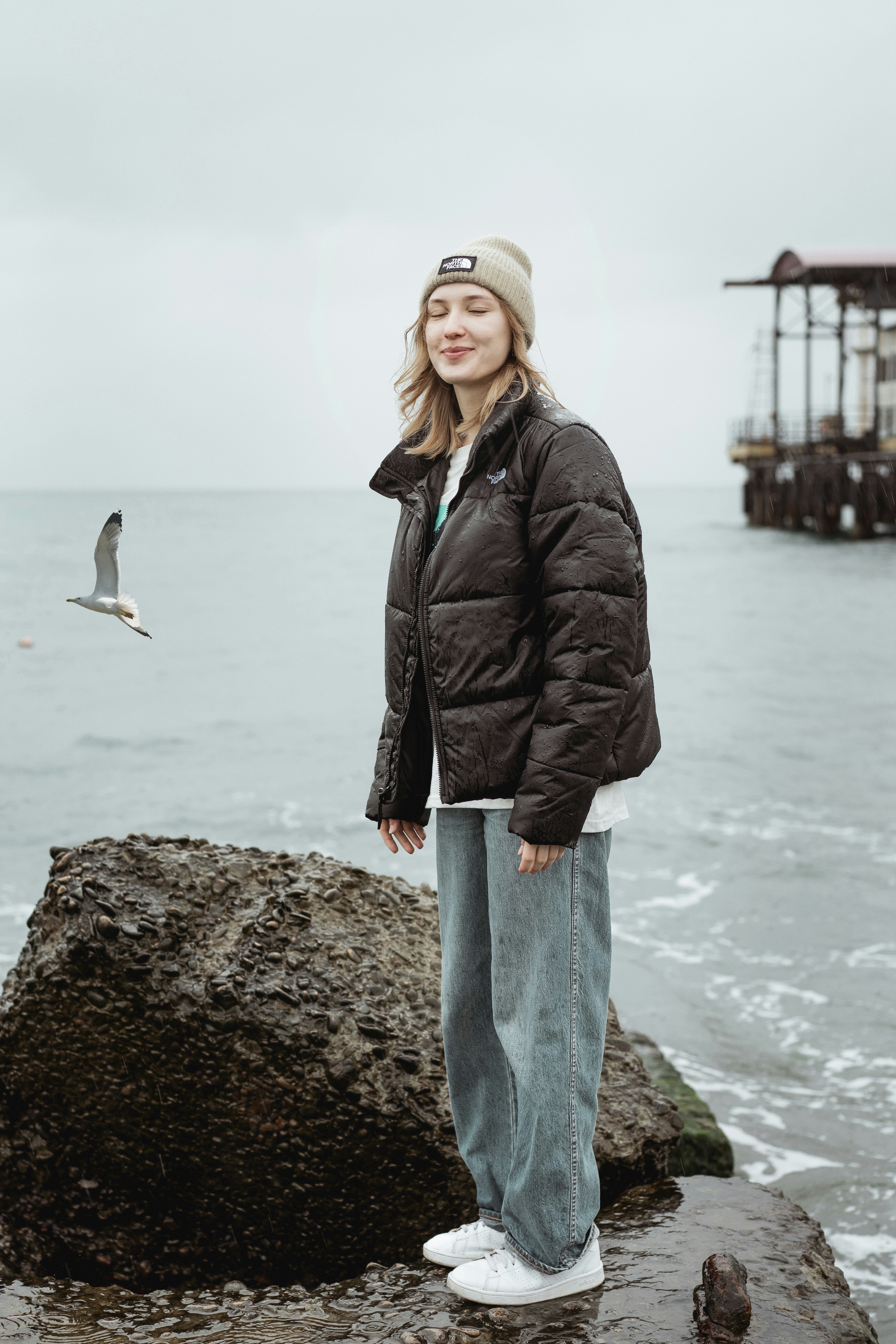 Woman in black leather jacket standing on rock near sea during daytime ...