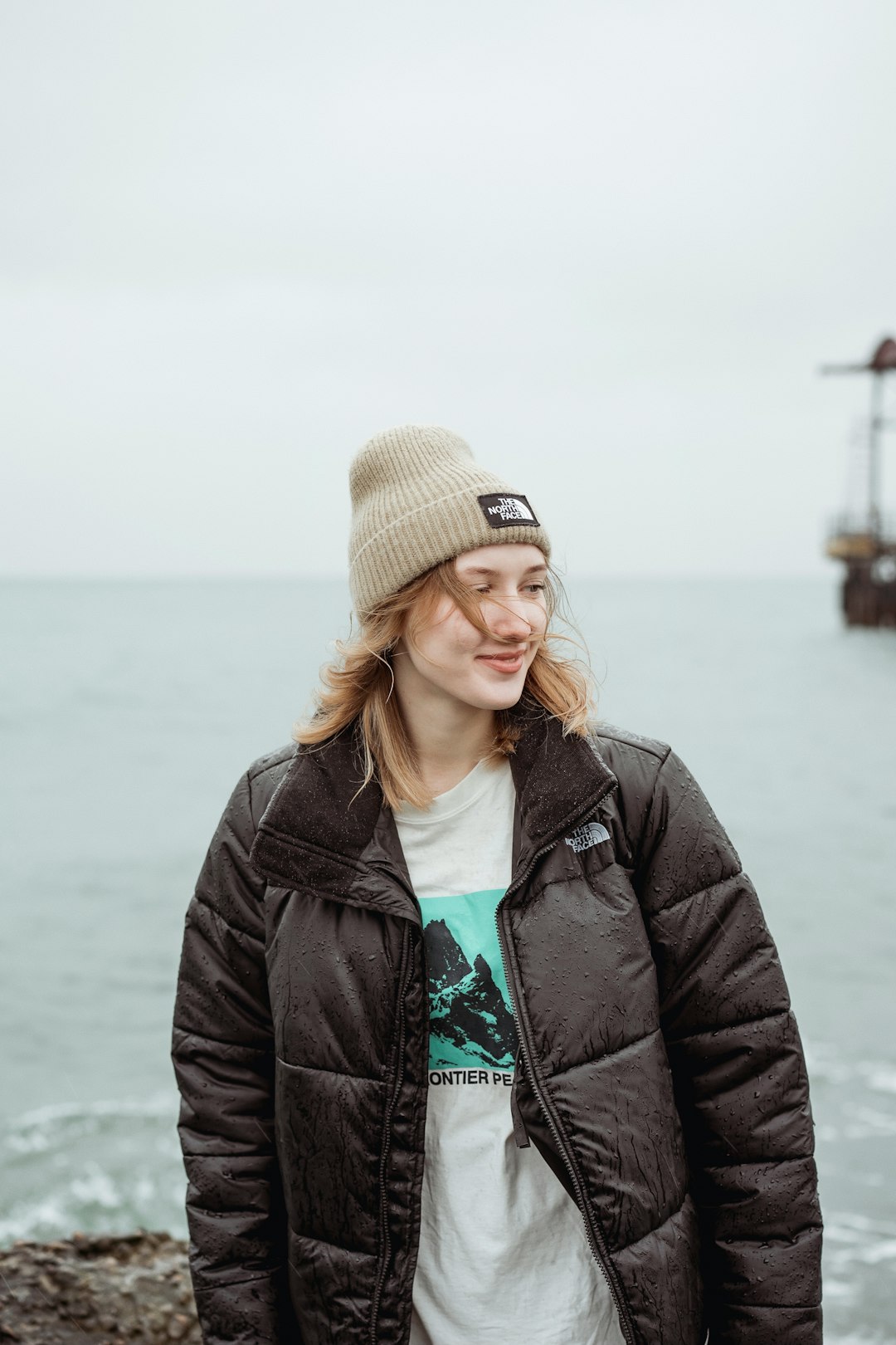 woman in black jacket and brown knit cap standing near body of water during daytime