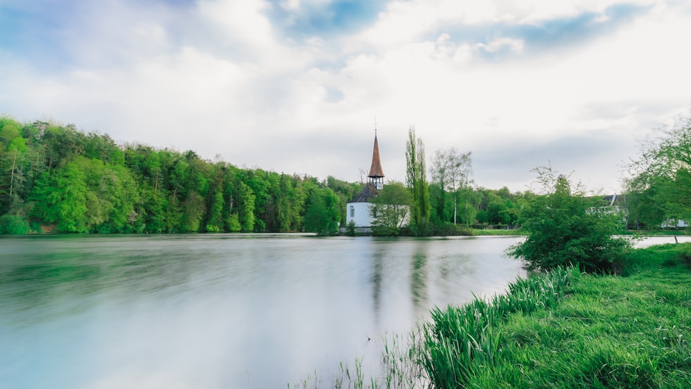 white and brown concrete building near green trees and lake under white clouds during daytime