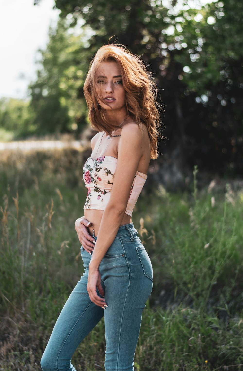 woman in white and red floral tank top and blue denim jeans standing on green grass