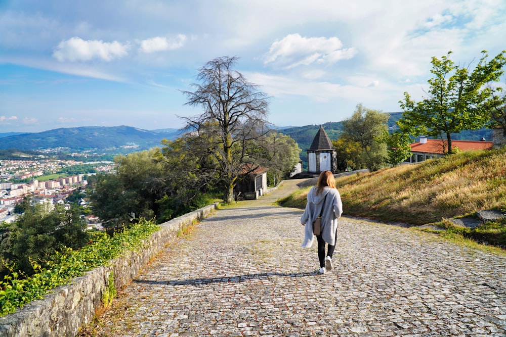 woman in white coat walking on pathway near green grass field during daytime