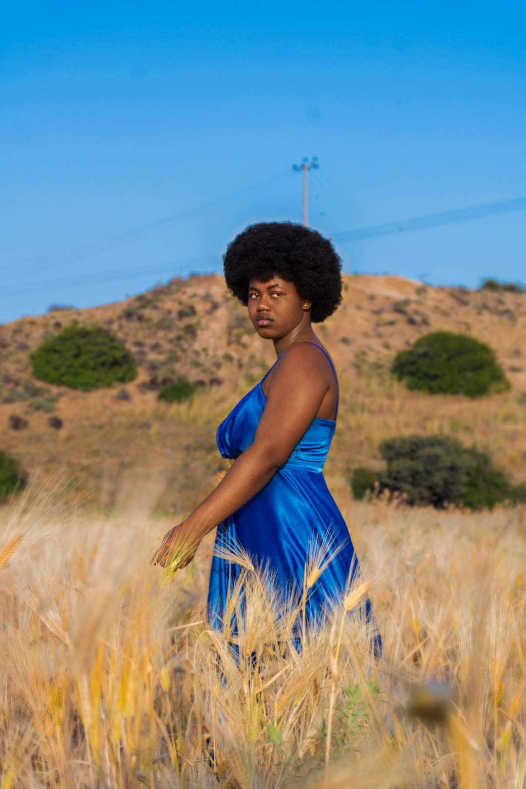 woman in blue spaghetti strap dress standing on brown grass field during daytime