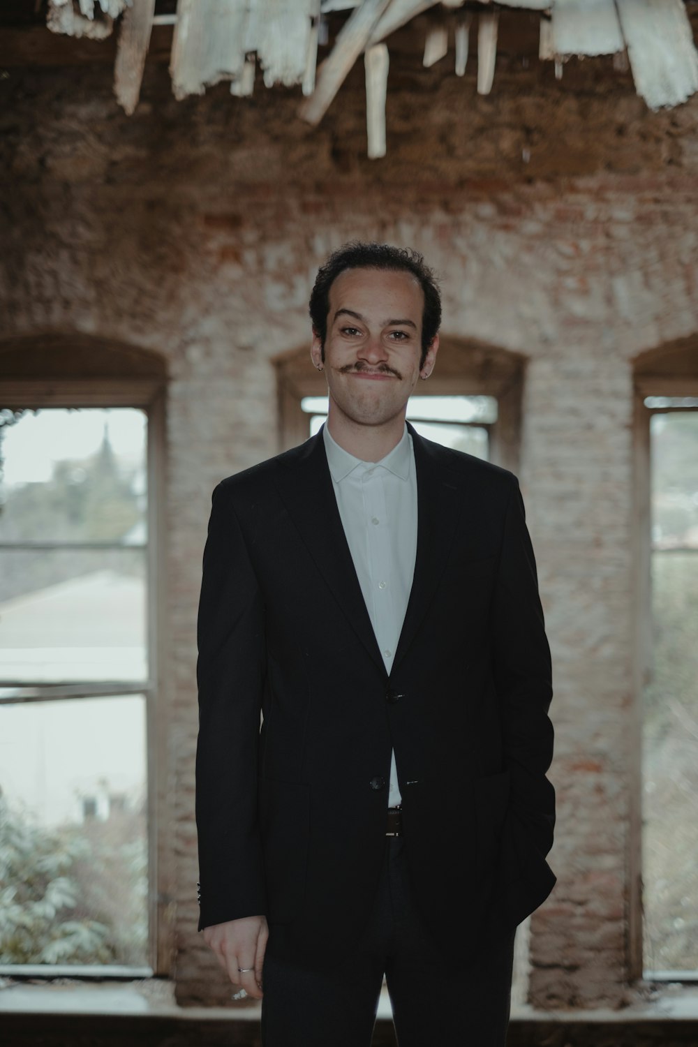 man in black suit jacket standing near brown brick wall