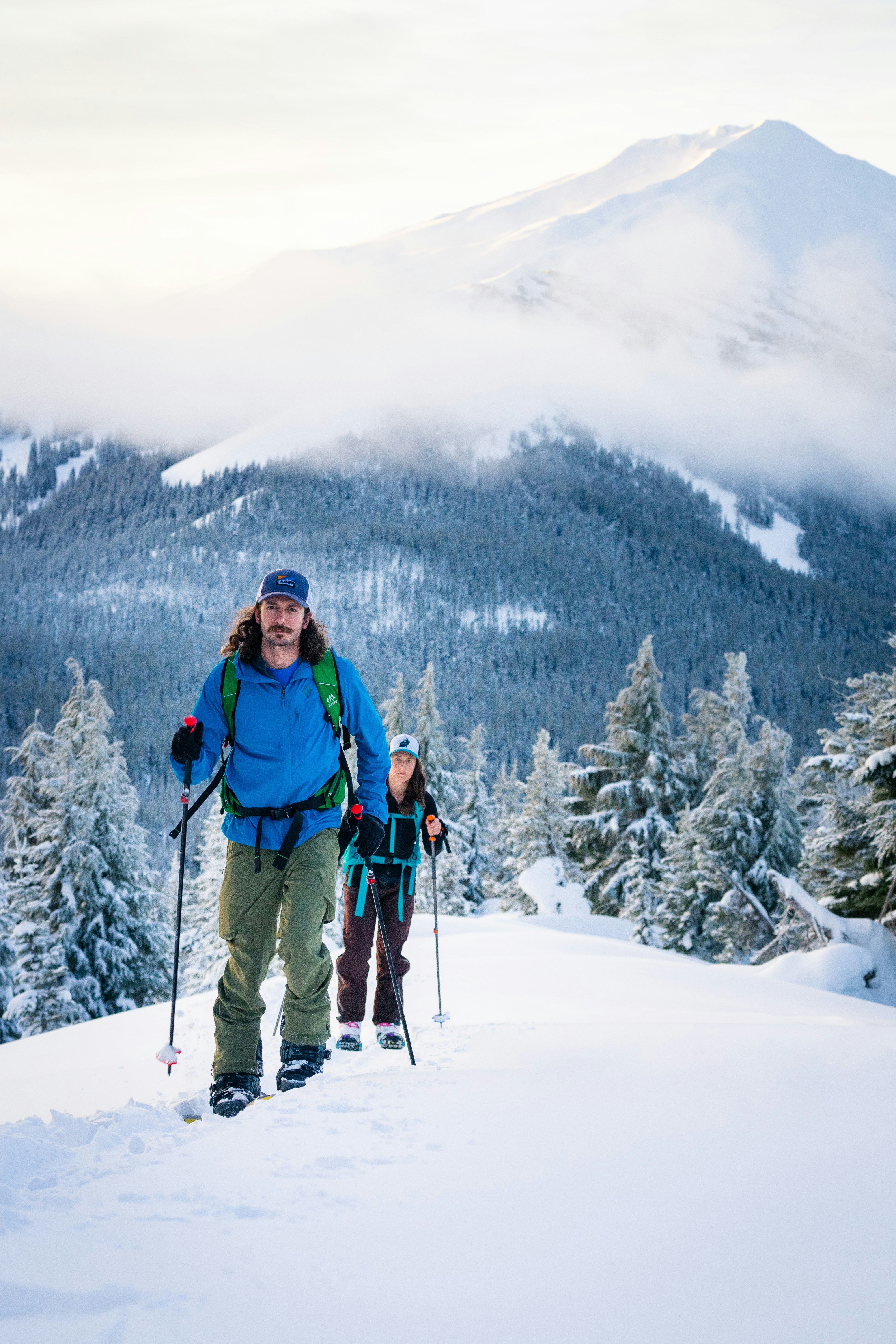 Hombre con chaqueta azul y mochila azul de pie en suelo cubierto de nieve