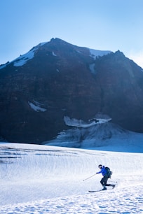 person in black jacket and blue denim jeans walking on snow covered ground near mountain during