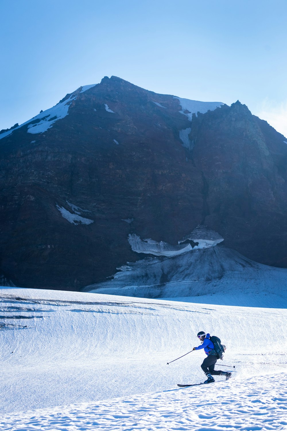 person in black jacket and blue denim jeans walking on snow covered ground near mountain during