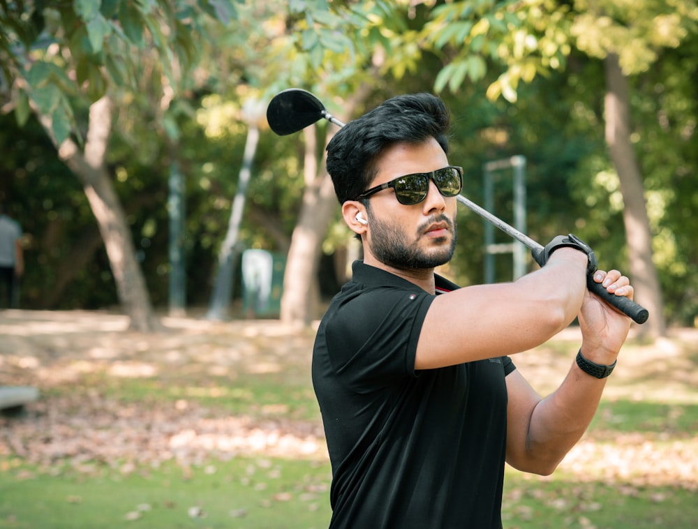 man in black crew neck t-shirt wearing black sunglasses holding black golf club during daytime