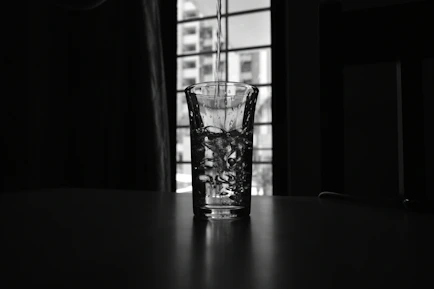 Close-up of sparkling clean water pouring into a glass beside a houseplant.