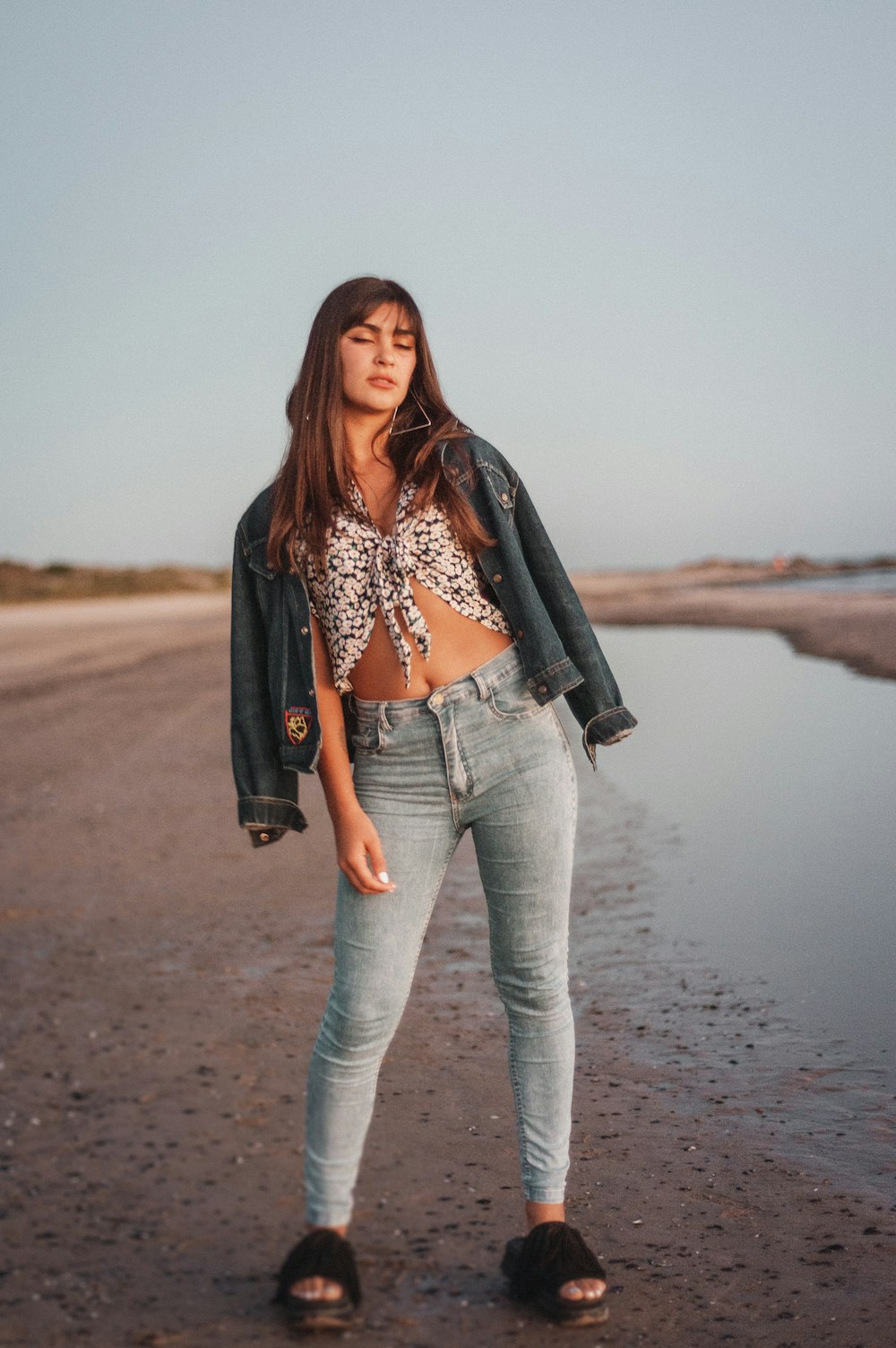 woman in black leather jacket and gray denim jeans standing on gray sand during daytime