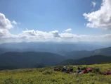 A panoramic view of a mountain trekking group resting with backpacks and scenic peaks behind.