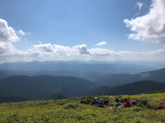 A vibrant snapshot of a group of travelers hiking through lush green mountains under a clear blue sky.