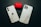 Two smartphones with marble-patterned cases are lying on a dark surface next to a red case with black designs. The phones have a minimal and sleek design with visible camera lenses.