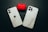 Two smartphones with marble-patterned cases are lying on a dark surface next to a red case with black designs. The phones have a minimal and sleek design with visible camera lenses.
