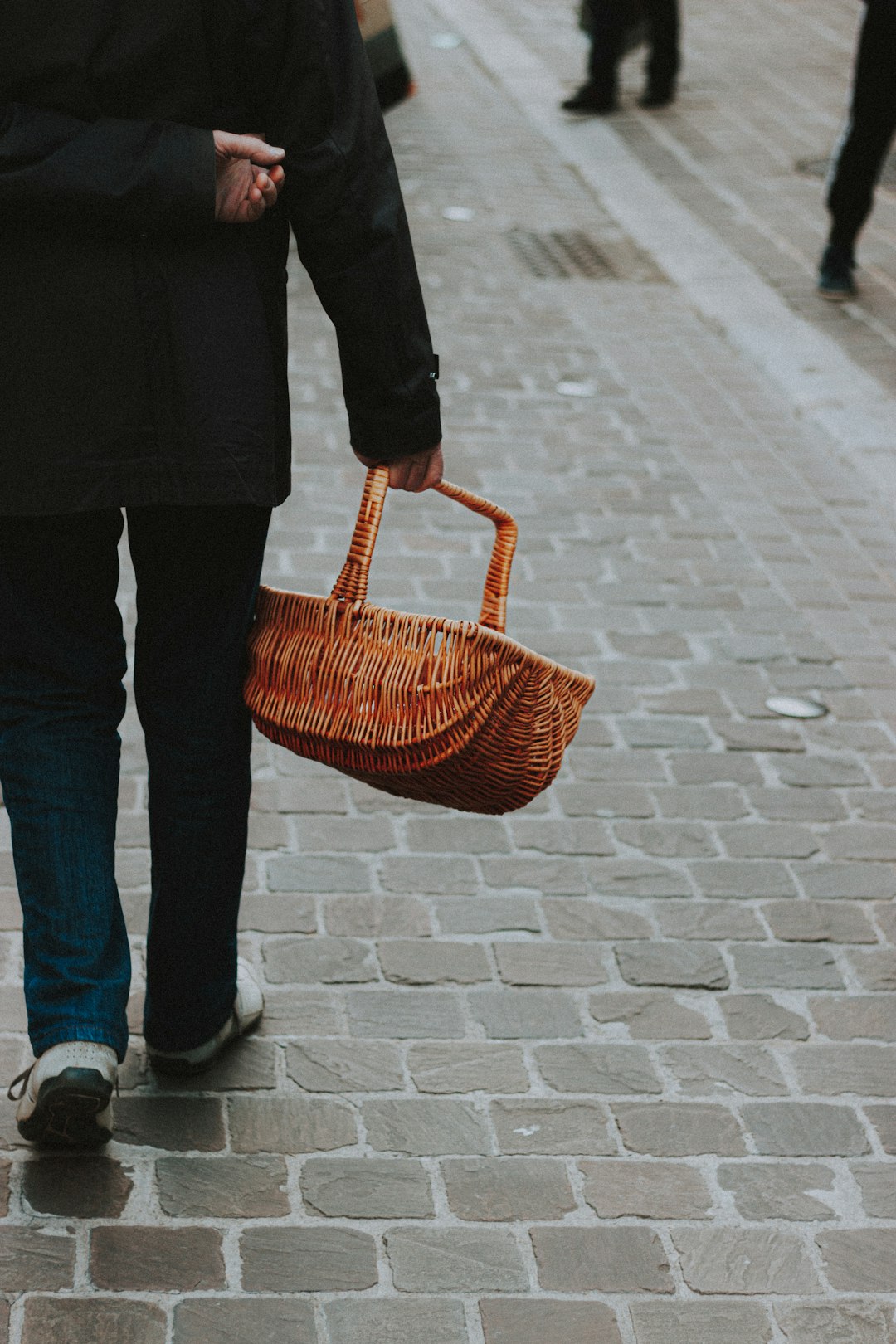 person in black jacket and blue denim jeans holding brown woven basket