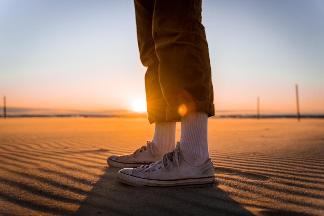person in blue denim jeans and white sneakers standing on brown sand during daytime