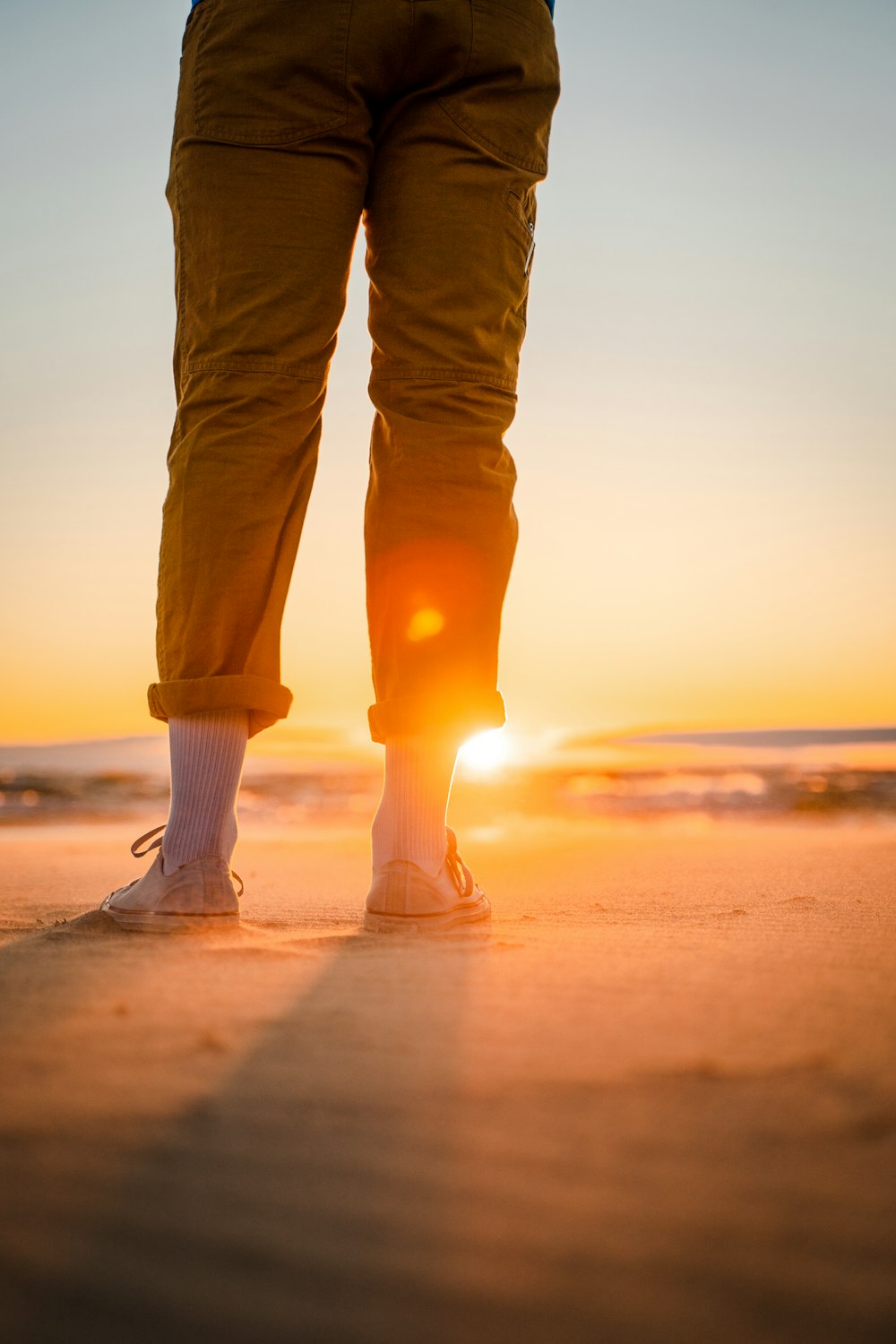 Person in braunen Hosen und weißen Socken, die bei Sonnenuntergang am Strand steht