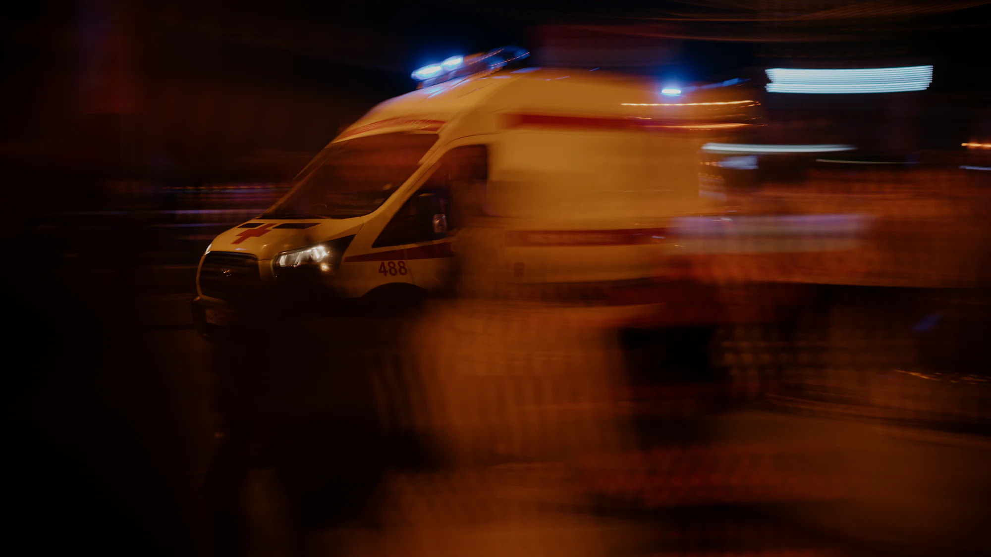 An ambulance running under blue lights on a wet street at night.