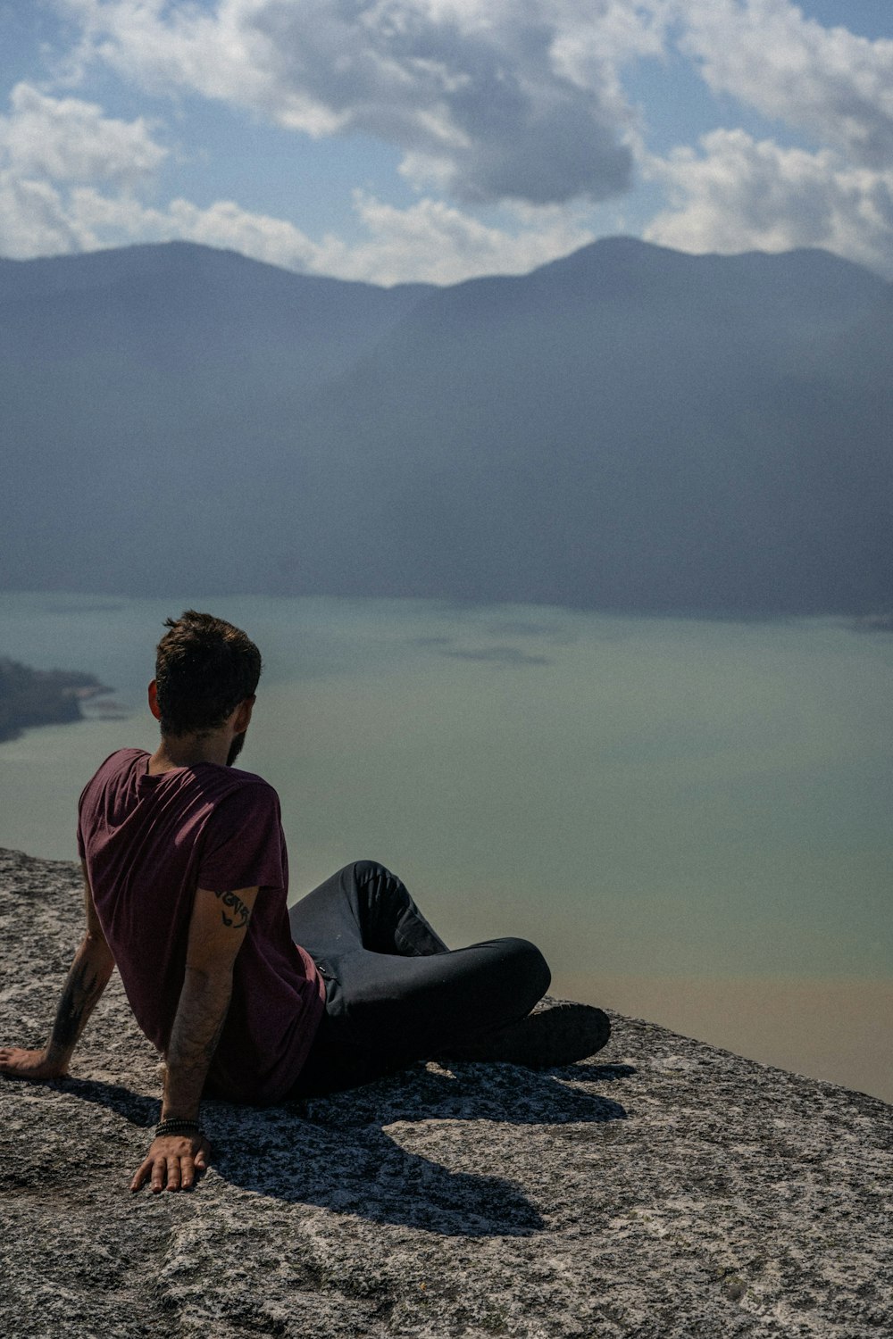 man in red hoodie sitting on rock near body of water during daytime