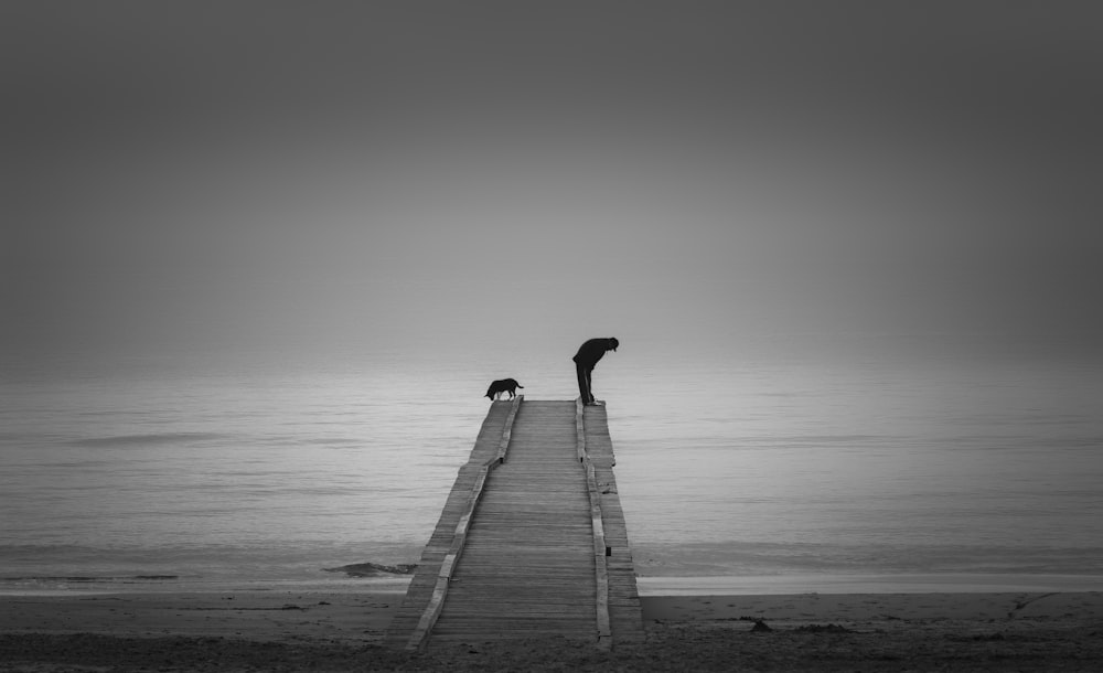 person walking on wooden dock in grayscale photography