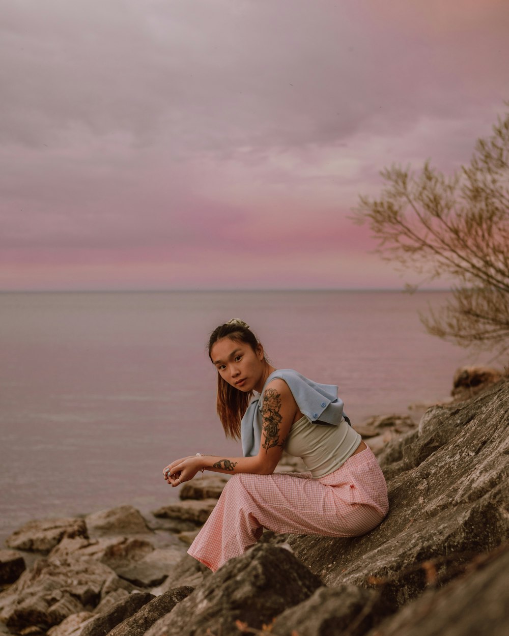 woman in white shirt sitting on brown rock near body of water during daytime