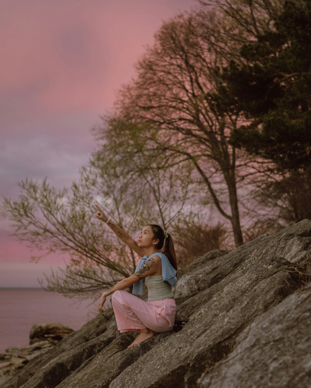 woman in blue t-shirt sitting on rock near body of water during daytime