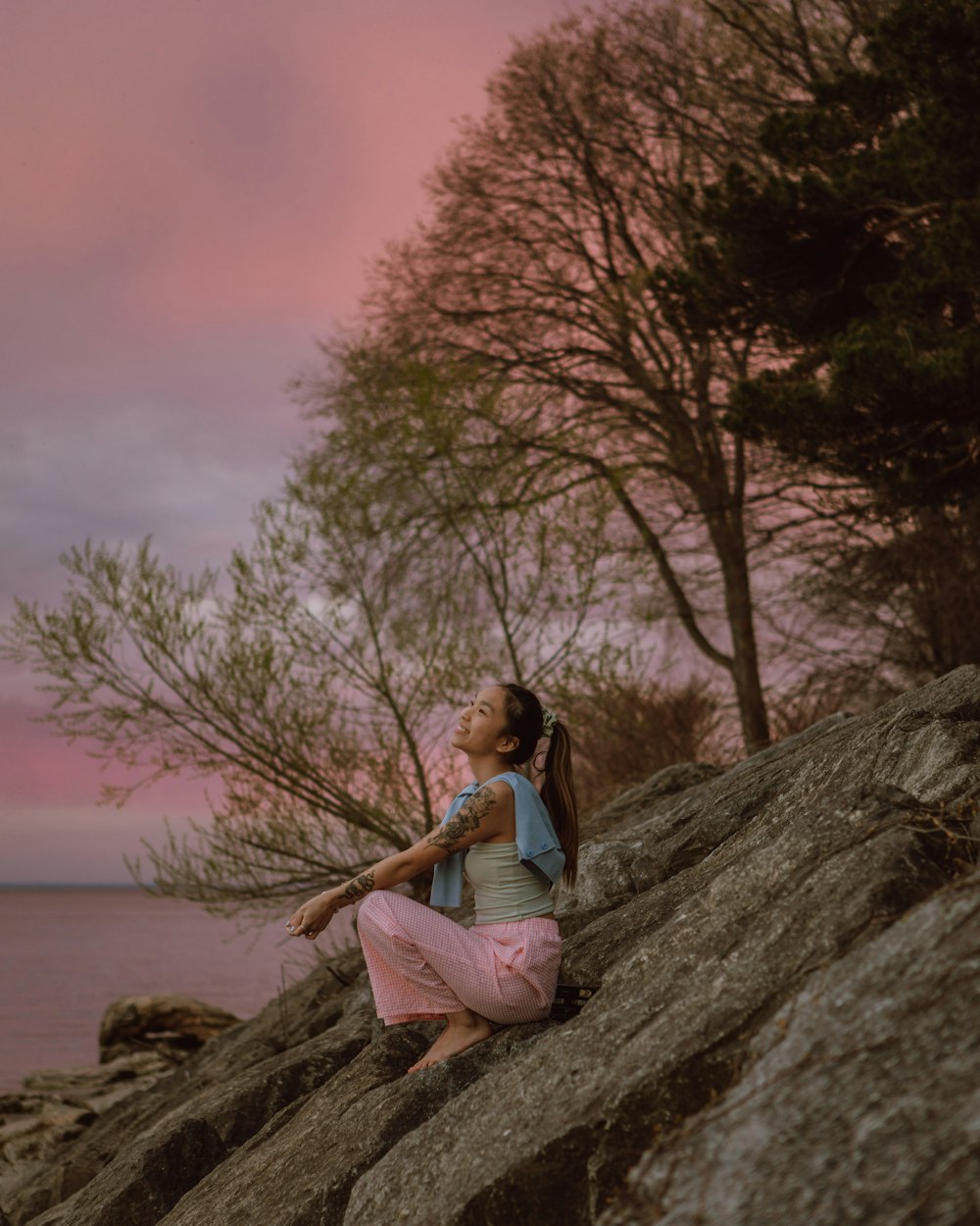 woman in black tank top sitting on brown rock near body of water during daytime