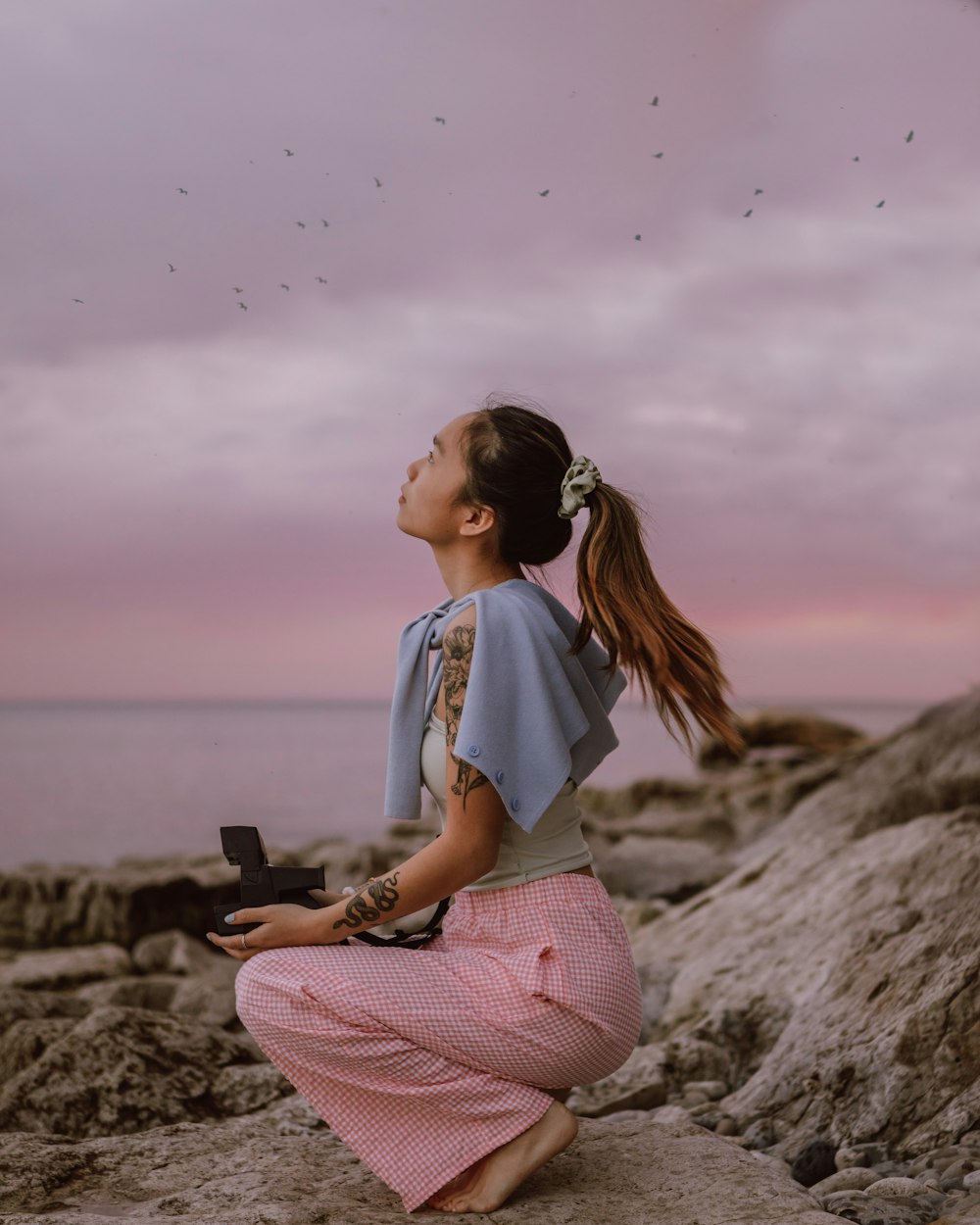 woman in white shirt and pink pants sitting on rock during daytime