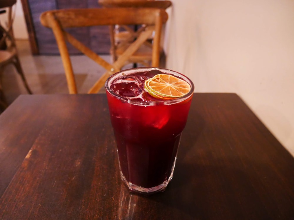 clear drinking glass with red liquid on brown wooden table