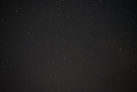 A dark, starry night sky with scattered, faintly visible stars on a backdrop of deep black.