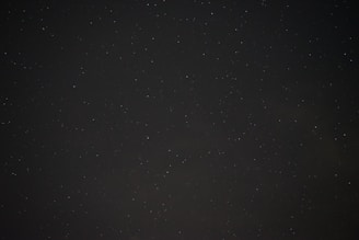 A dark, starry night sky with scattered, faintly visible stars on a backdrop of deep black.