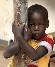 boy in yellow and red polo shirt holding brown wooden stick