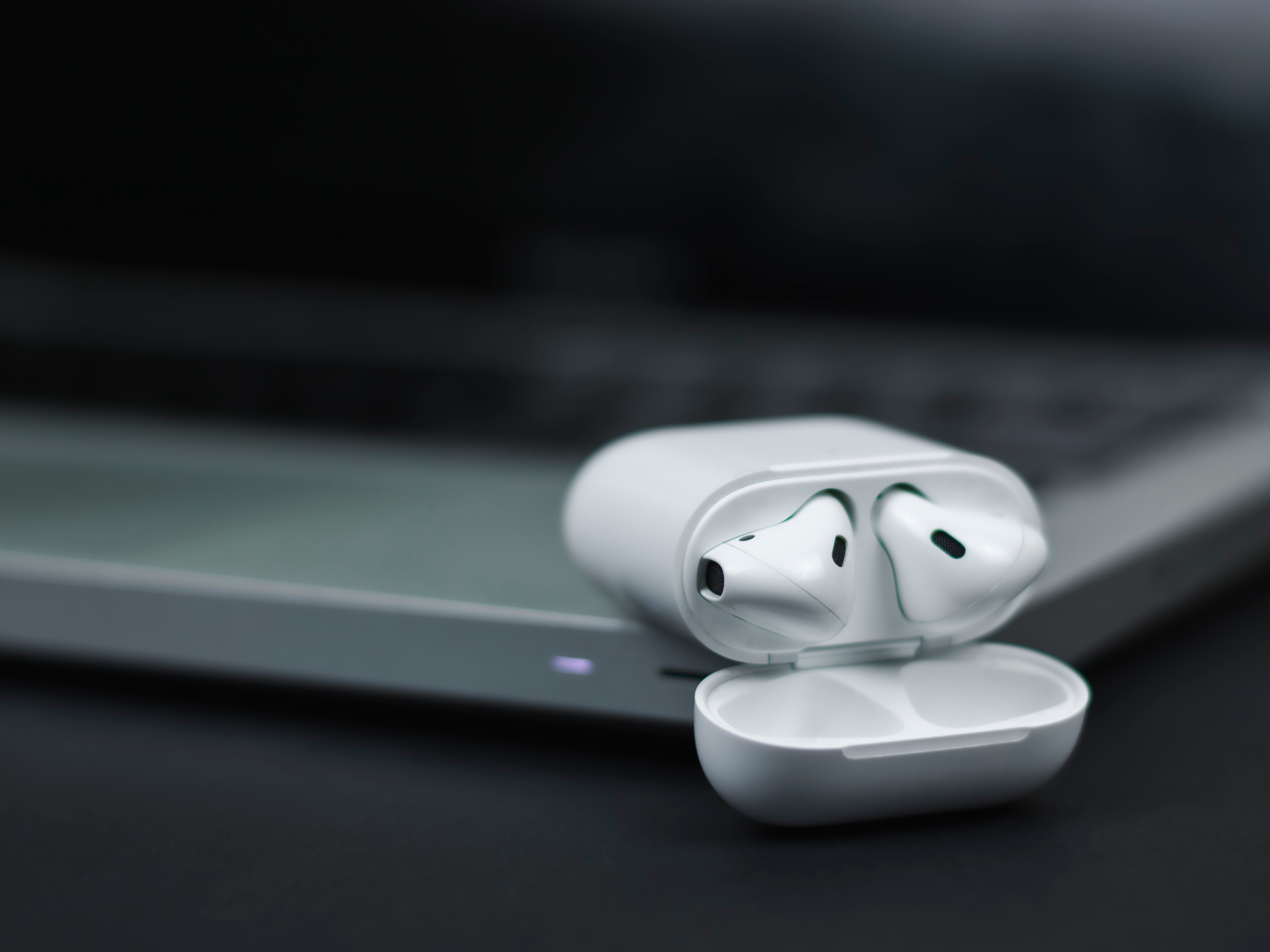 close up of wireless earbuds charging case next to a modern laptop