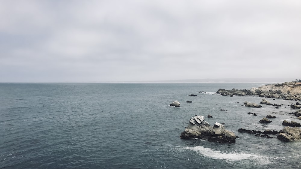 rock formation on sea under white clouds during daytime