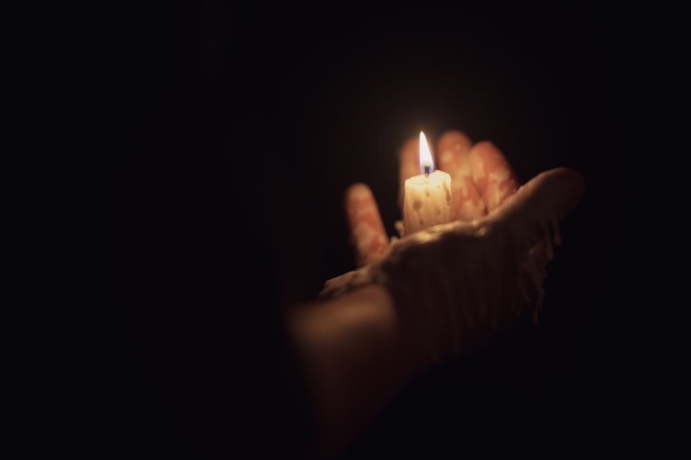 person holding lighted candle in dark room