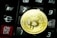 A golden Bitcoin coin is placed on a black calculator. The calculator keys are visible, including a red ON/CA button and various numbers and symbols, such as a Euro symbol.