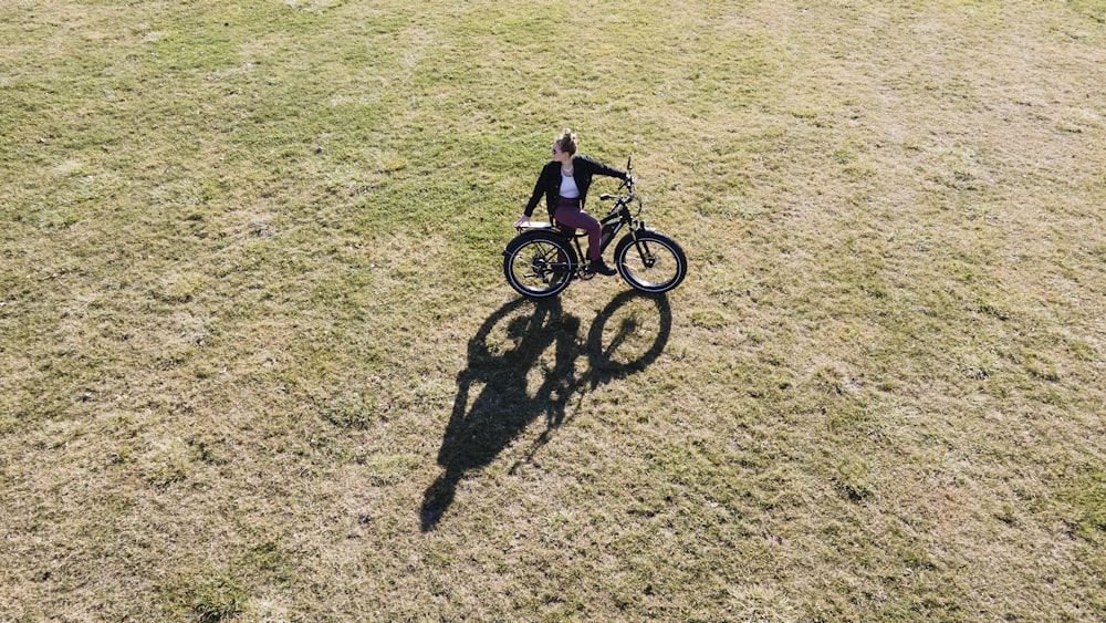 昼間、緑の芝生原で自転車に乗るピンクのジャケットを着た女の子