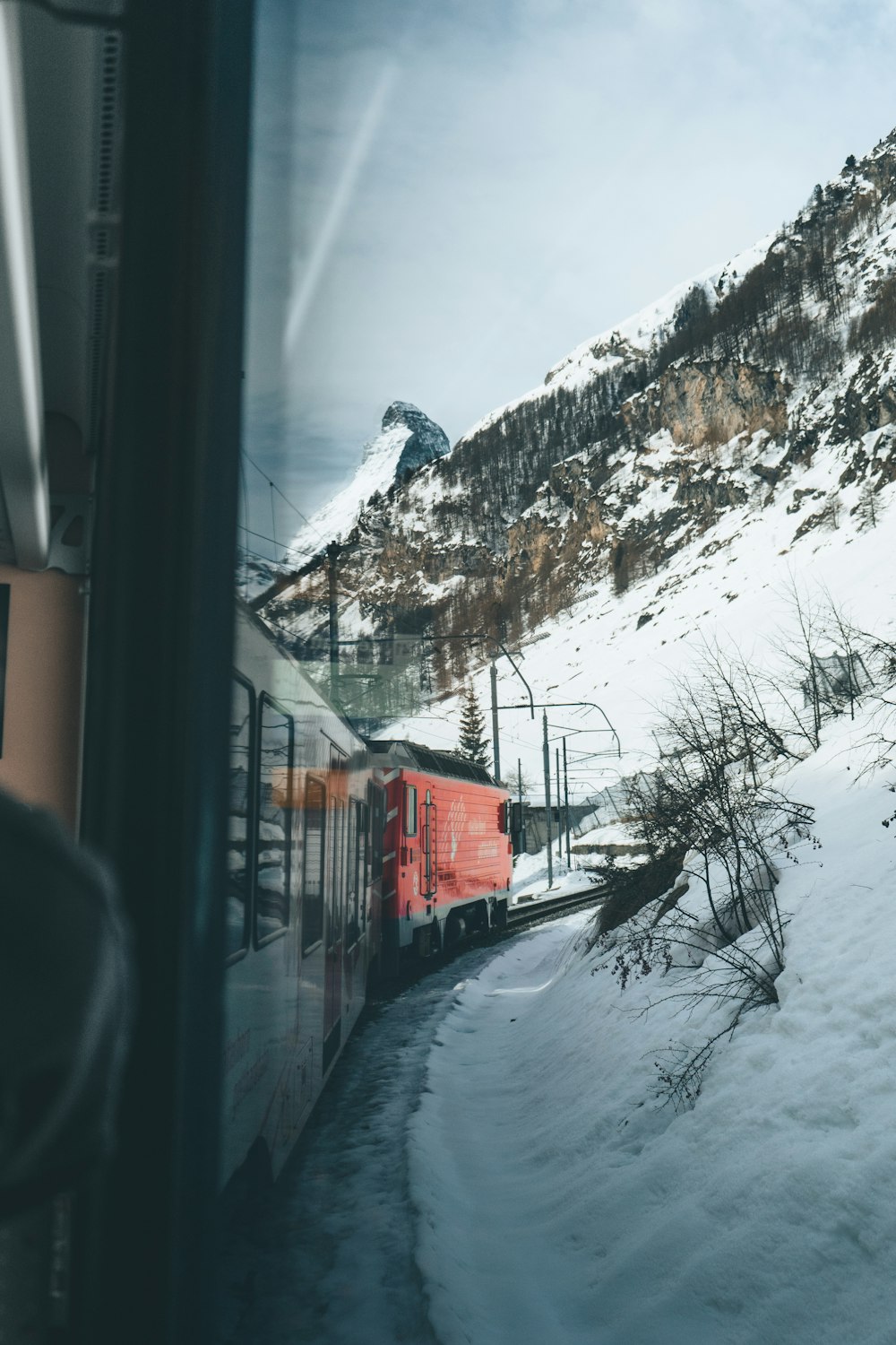 昼間、雪山近くの線路を走る赤い列車