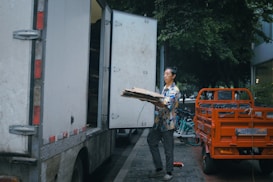 man in orange and black jacket and black pants standing beside white truck during daytime