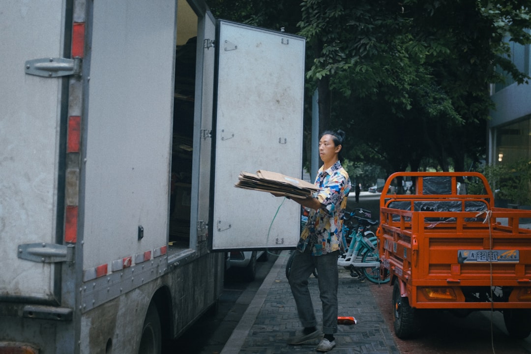 man in orange and black jacket and black pants standing beside white truck during daytime