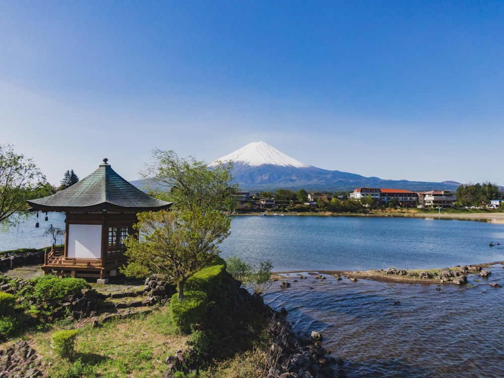 昼間の青空の下、湖と山の近くの茶色と白の家