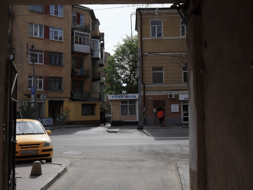 昼間、茶色のコンクリートの建物の脇に停車する黄色い車