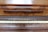 A wooden piano with a rich, textured finish displays a row of white and black keys. The name 'Franz Goetze' is engraved above the keys on a panel with a polished wood grain surface, suggesting an elegant and classical instrument.