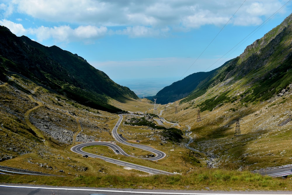 gray asphalt road between green mountains under blue sky during daytime