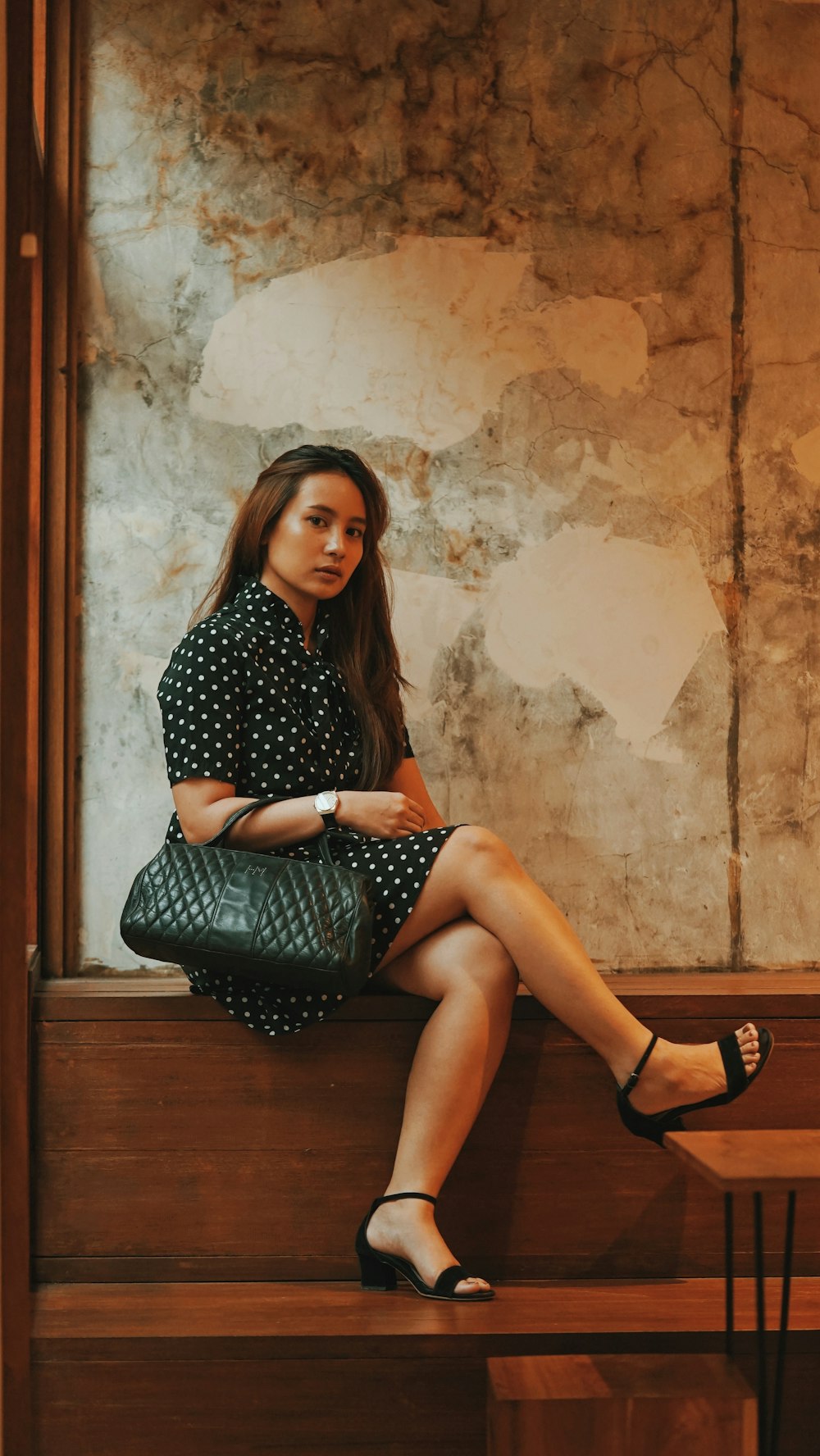 woman in black and white polka dot dress sitting on brown wooden seat